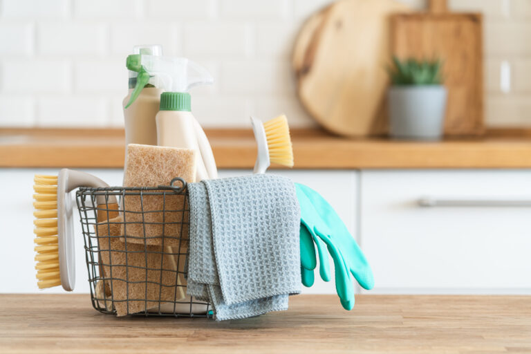 cleaning basket with rags, cleaner, brush in clean kitchen